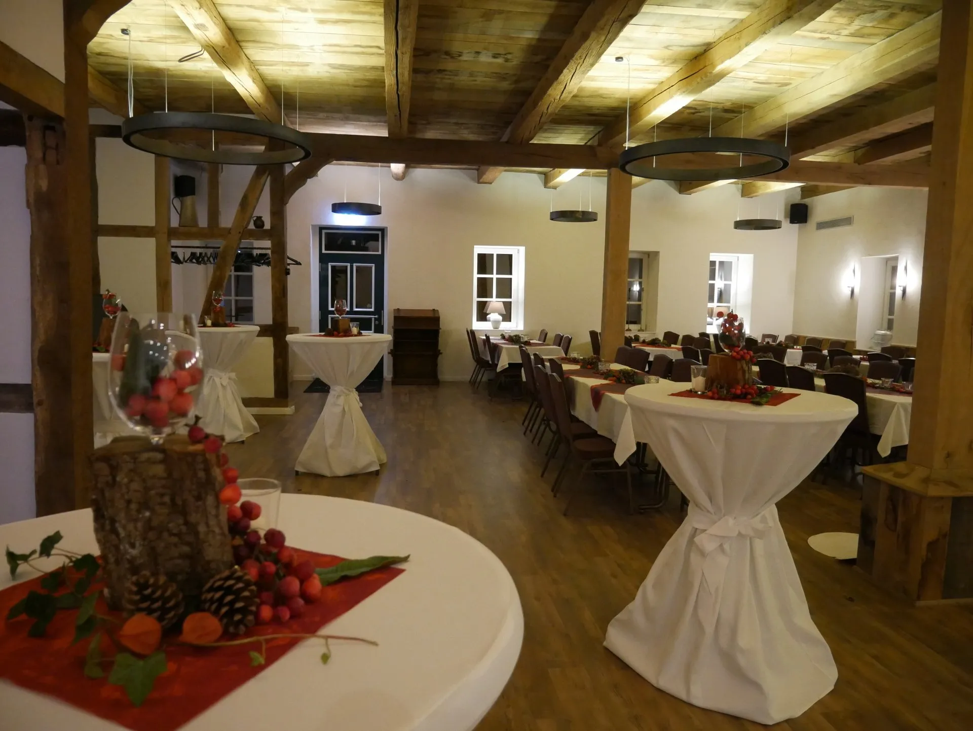 Die Party- und Eventlocation ist festlich geschmückt mit weißen Hussen auf Stehtischen und roter Deko.