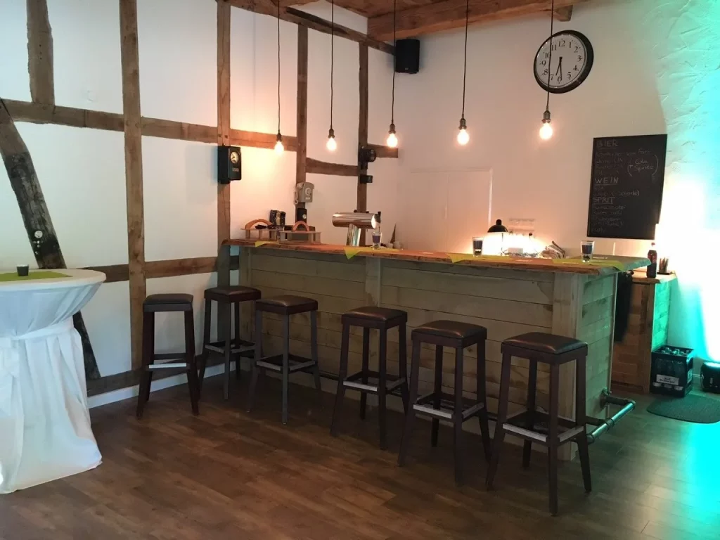 In der Party- und Eventlocation gibt es eine Theke mit Barhockern, Tafel und einer großen Uhr im Hintergrund.